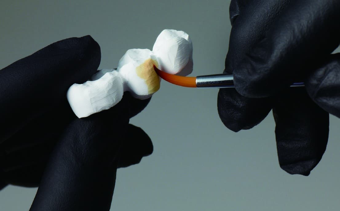 Lab technician in the USA staining a zirconia bridge by hand